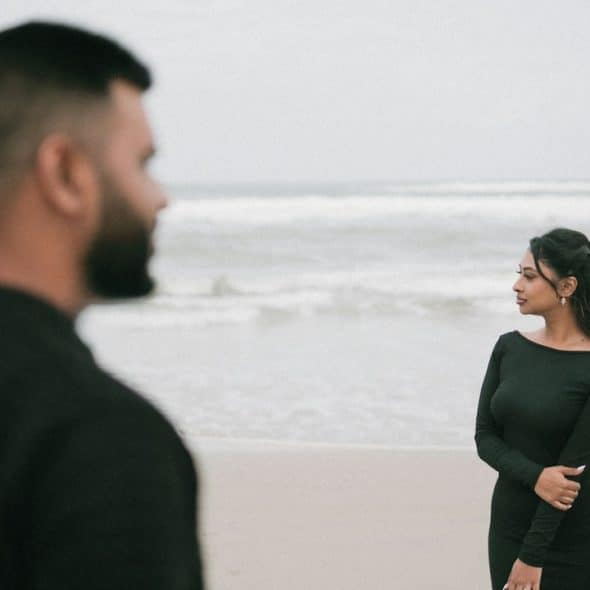 A couple on the beach are facing the ocean.