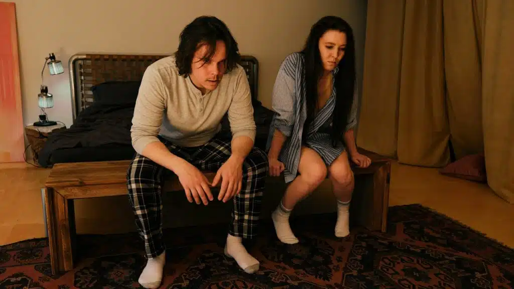 A man and a woman are sitting on a bed.