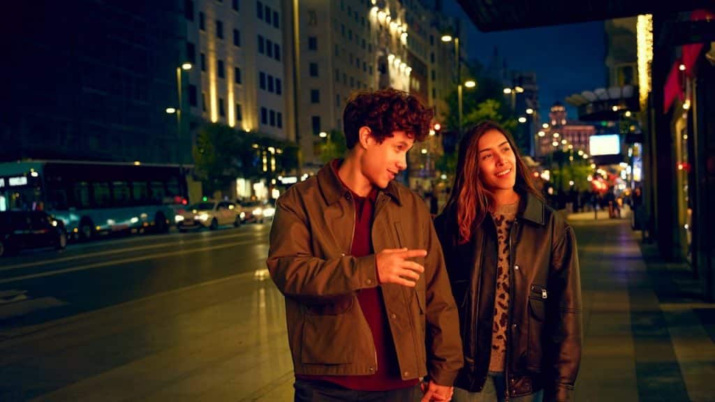 A couple walking through a street at night.