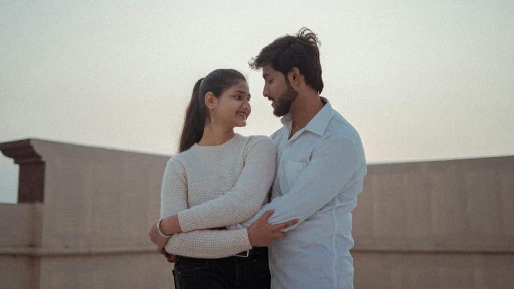 A couple hugging each other while standing on the rooftop of their home.