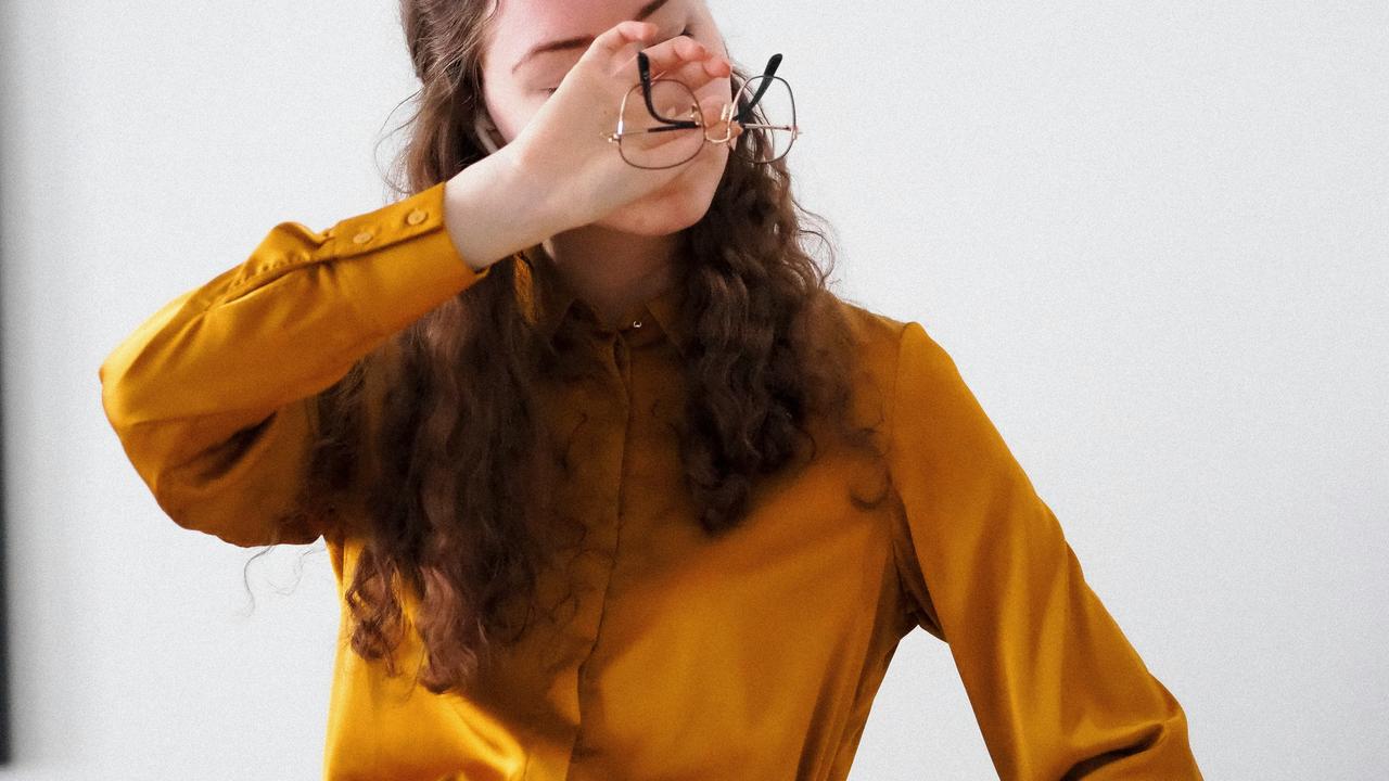 A woman holding her glasses and rubbing her eyes.