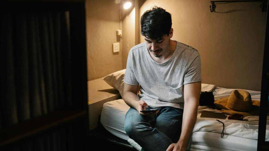 A man sitting on a bed looking at his phone.