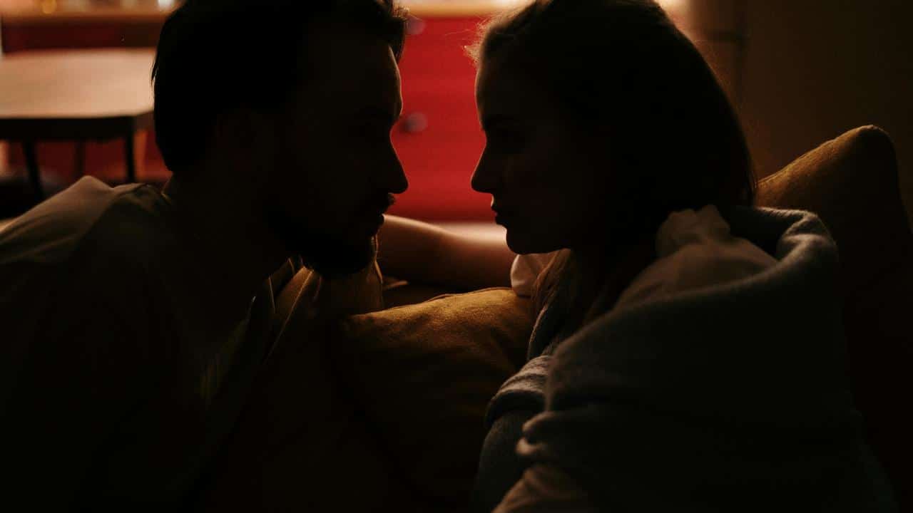 A couple sitting close and facing each other in dim light.