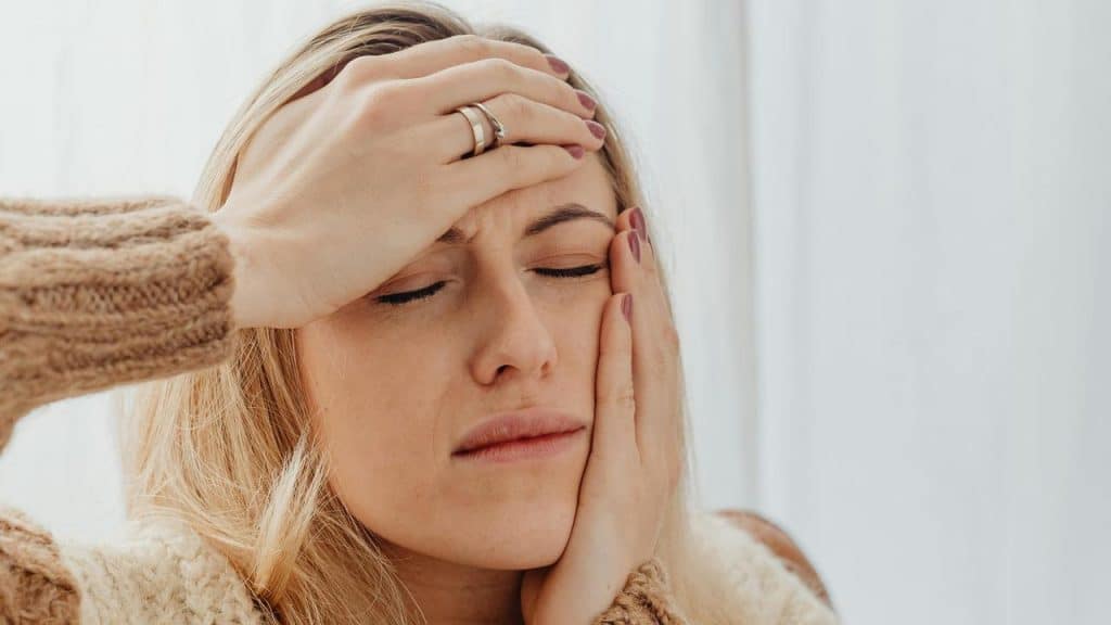 A woman holding her head with eyes closed.