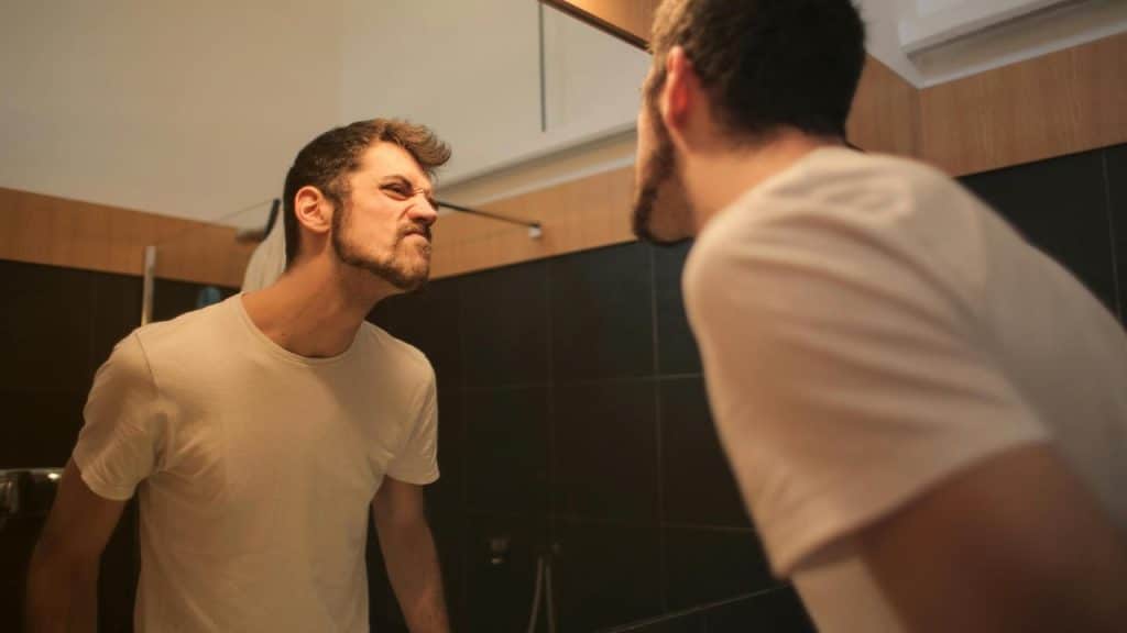 A man making an angry face at his reflection in a bathroom mirror.