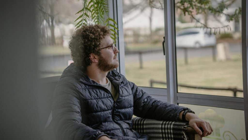 A man with curly hair sitting by a window and looking outside.
