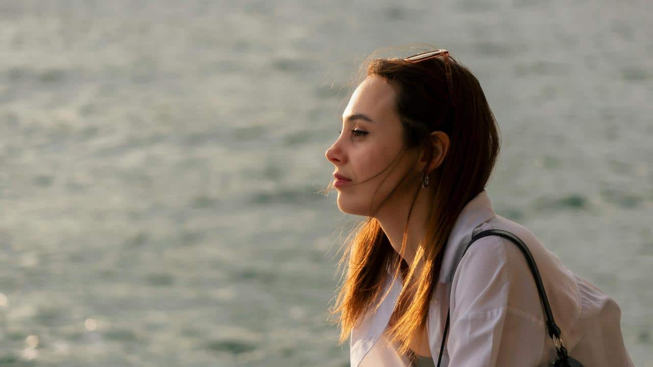 A woman gazing thoughtfully over the water in warm sunlight.