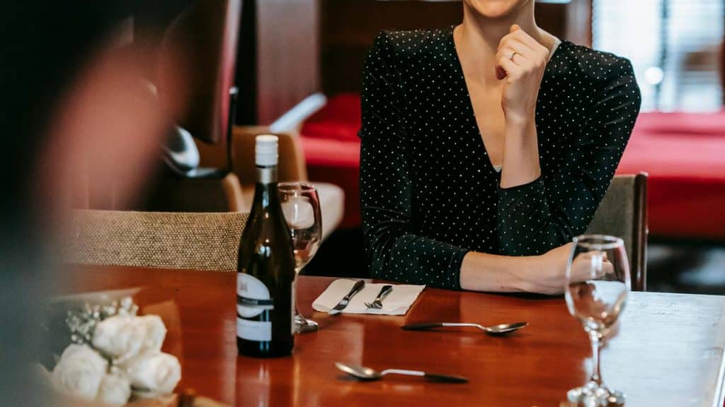 A woman in a black polka dot dress sitting at a restaurant table with wine.