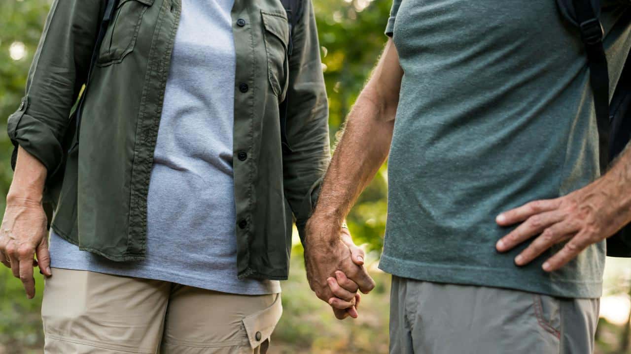 A couple holding hands while walking outdoors in a green, natural setting.