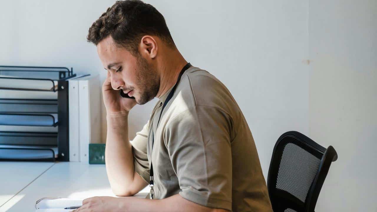 A man talking on the phone while sitting at a desk.