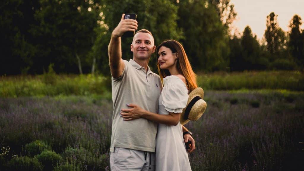 A man and woman pose for a selfie in a field of purple lavender flowers.
