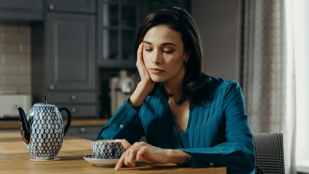A woman sitting at a table looking down thoughtfully beside a teacup.
