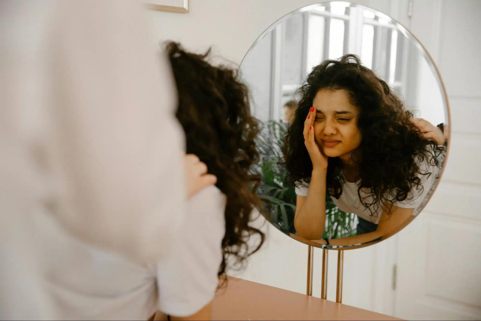 A woman holding her head in front of the mirror.