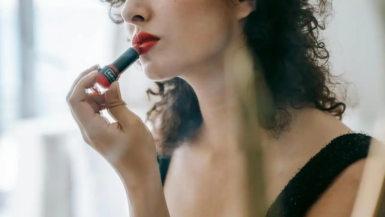 A woman applying red lipstick in front of a mirror.