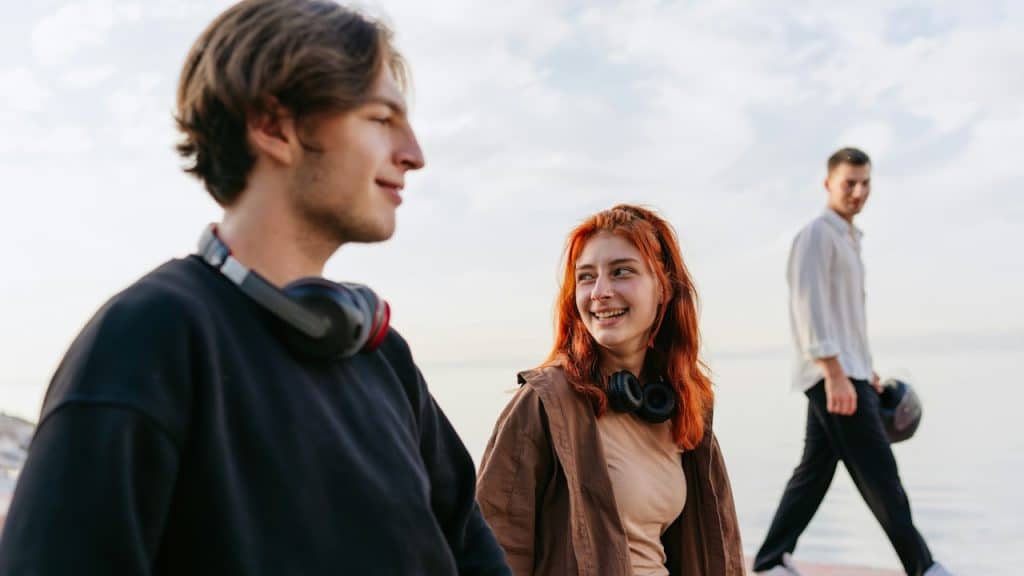 A couple of people are wearing earphones, and a man is walking in the background.