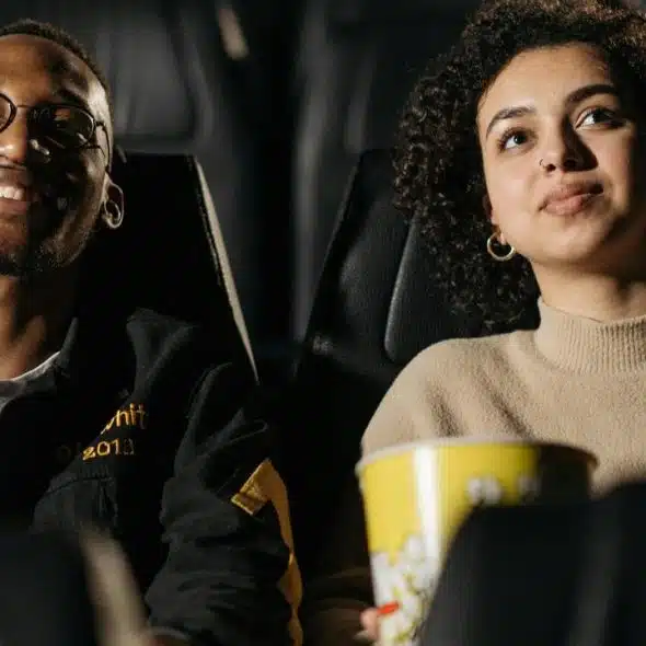 A couple sitting in a movie theater watching a film with popcorn.