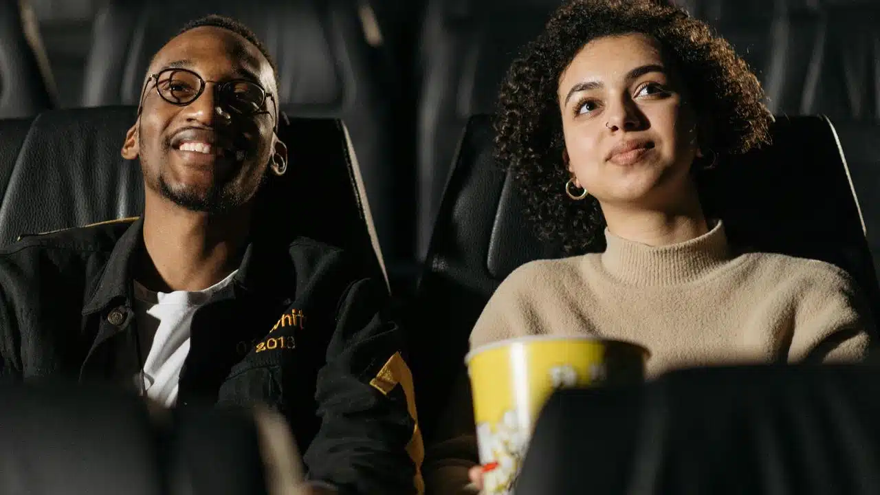 A couple sitting in a movie theater watching a film with popcorn.