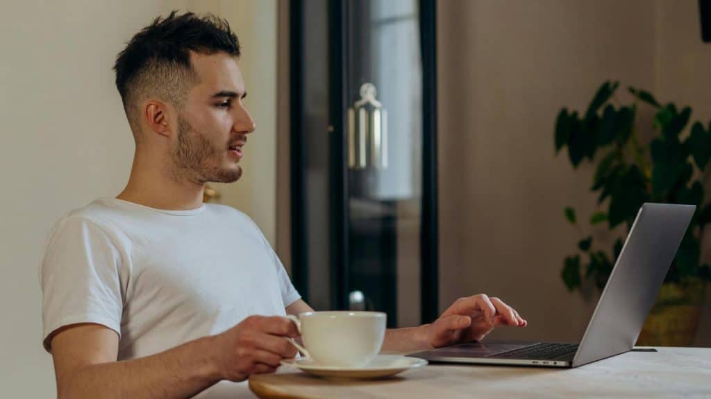 A man using a laptop while holding a cup at a table.