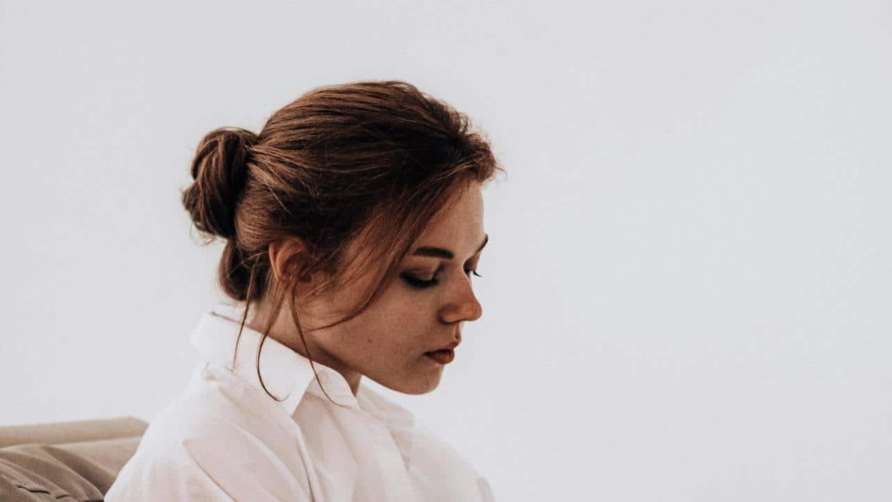 A woman with her hair in a bun looking down with a thoughtful expression.