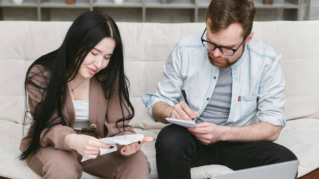A couple sitting on a couch reviewing receipts and taking notes together.