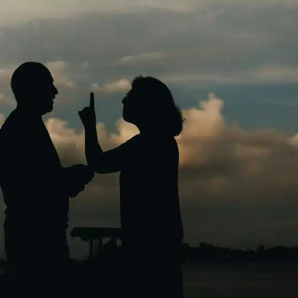 A silhouetted man and woman facing each other, one gesturing with a raised finger.