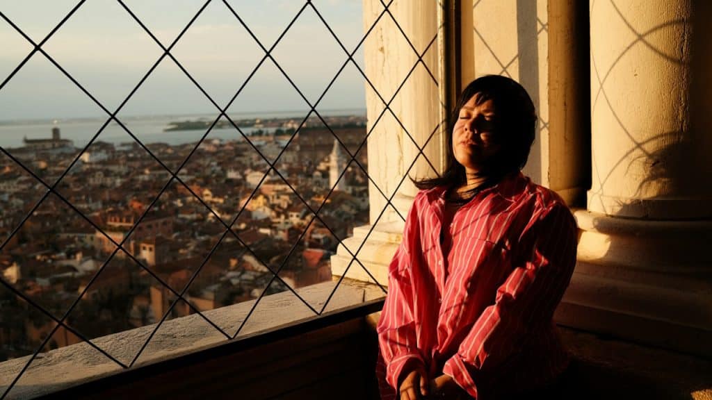 A depressed woman leaning on the wall near a window.