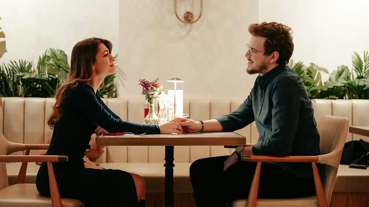A couple holding hands and looking at each other while sitting at a restaurant table.