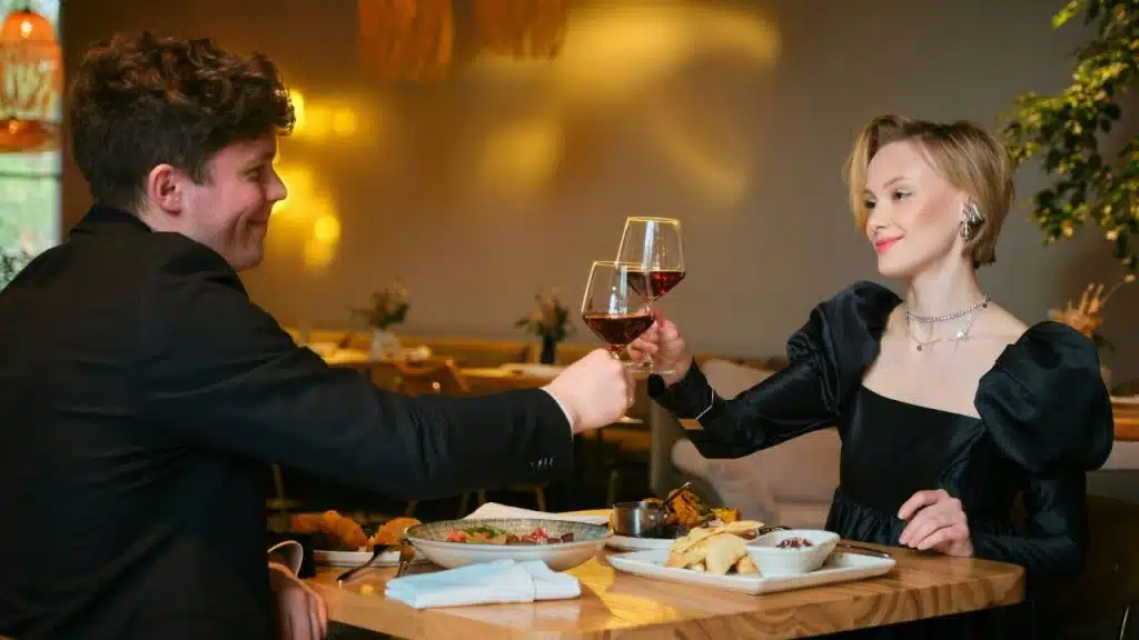 A man and woman in formal attire toast with red wine glasses over dinner.