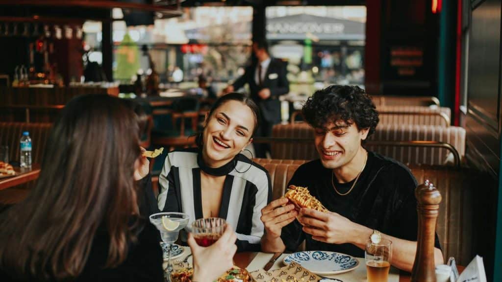 A group of friends sit at a restaurant table, laughing and sharing a meal.