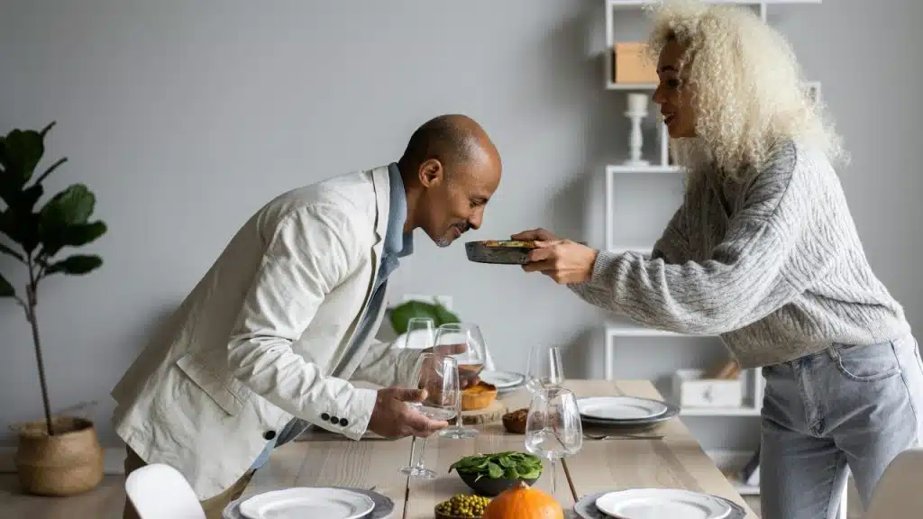 A woman serves a plate of food to a man leaning in at a table.