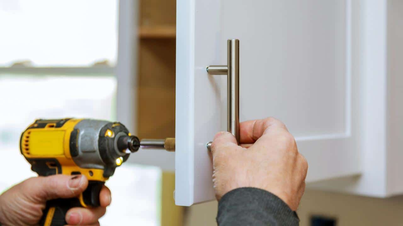A person using a drill to install a handle on a cabinet door.