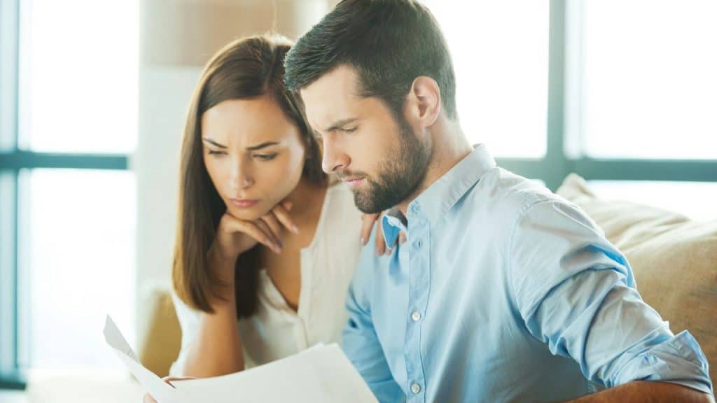 A man and woman look closely at a document with serious, focused facial expressions.