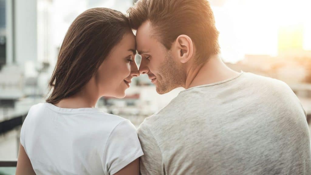 A man and woman lean their foreheads together in a close profile shot outdoors.