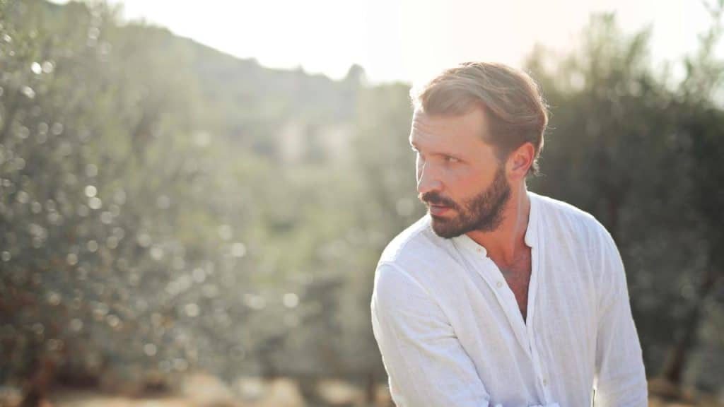 A man in a white shirt looking to the side outdoors.