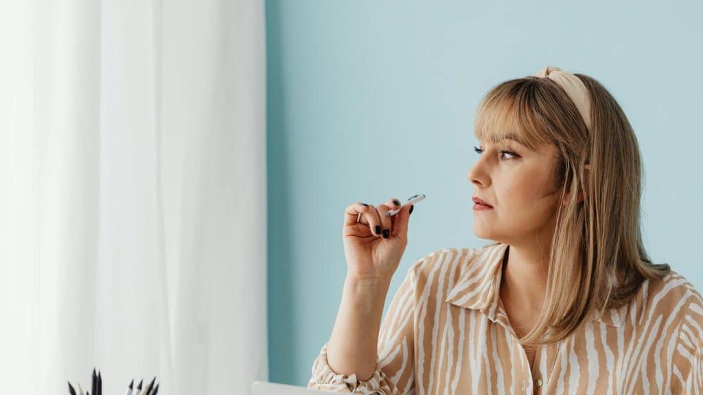 A woman holding a pen while looking thoughtfully to the side.