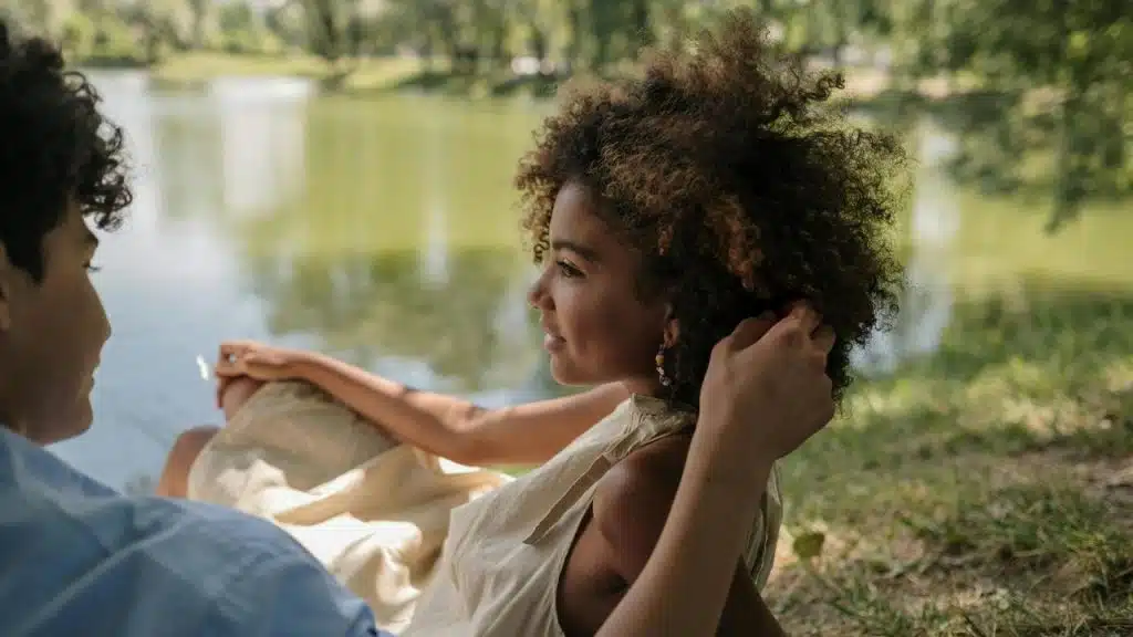 A couple sitting by a lake with one person touching the other's hair