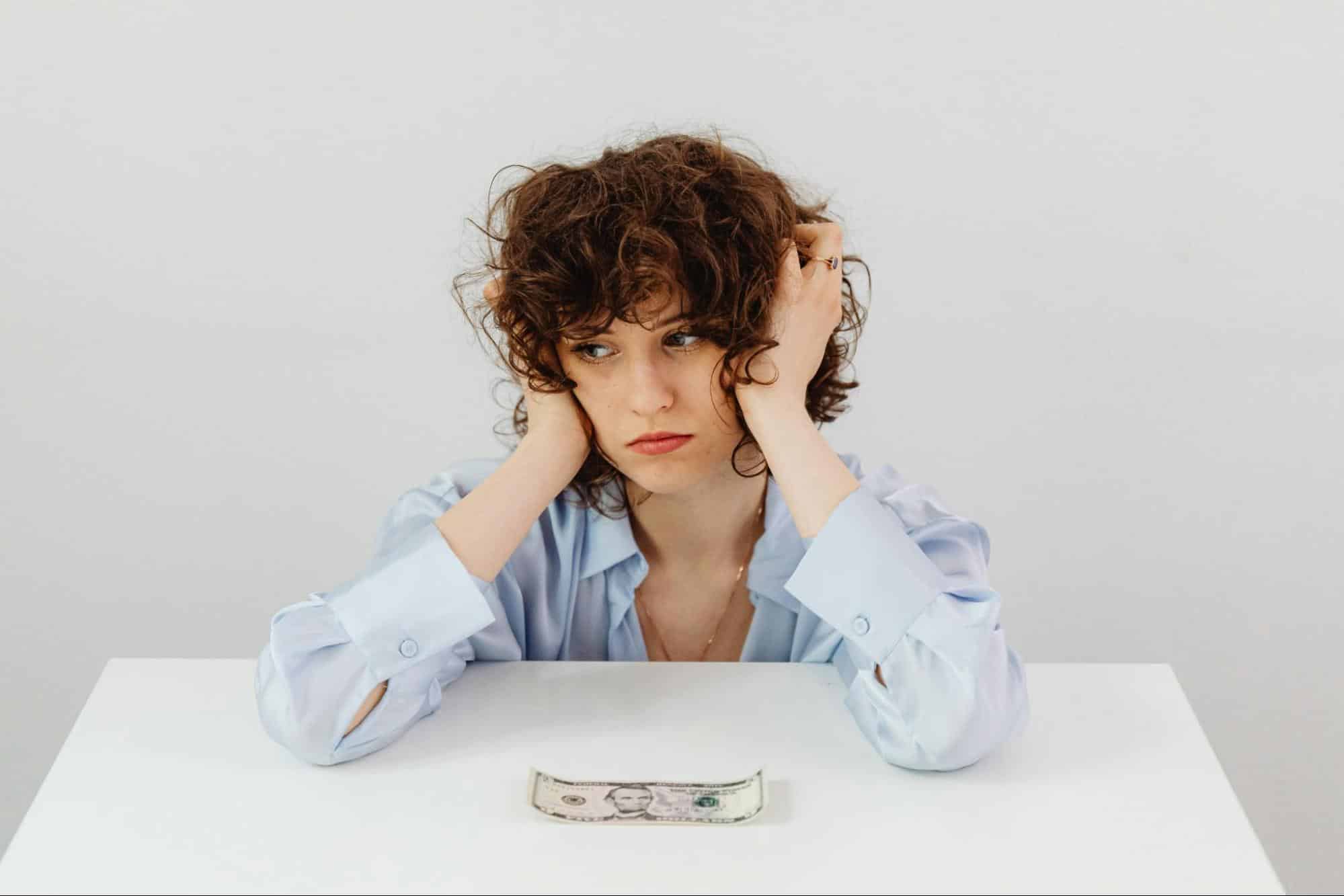 A woman holding her head by the money on the table.