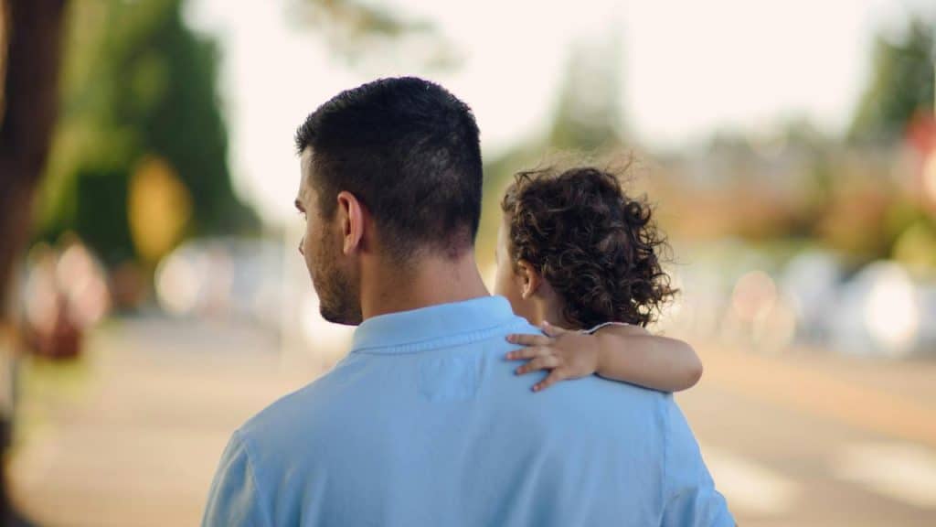 A man carrying a child on his shoulder outdoors.