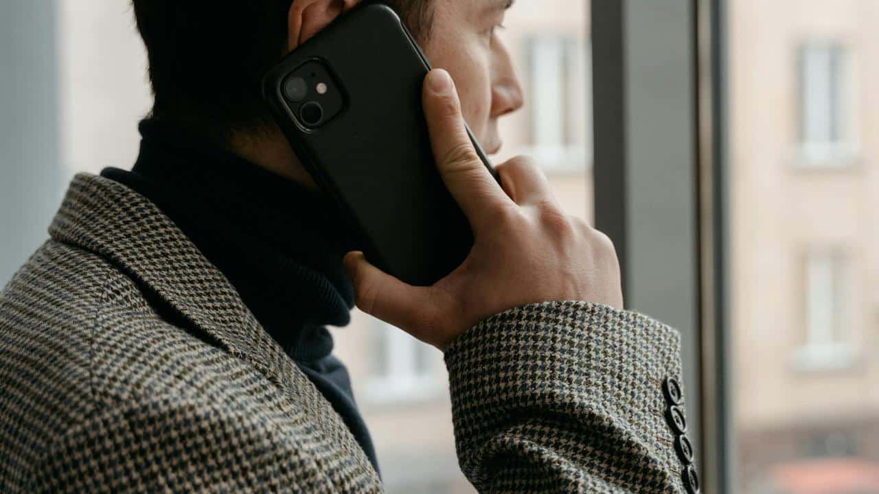A man holding a phone to his ear while standing by a window.