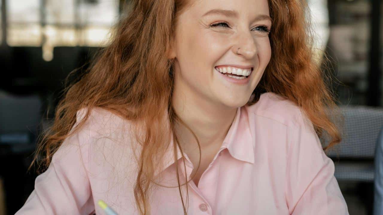 A woman with long red hair smiles while sitting at a table.