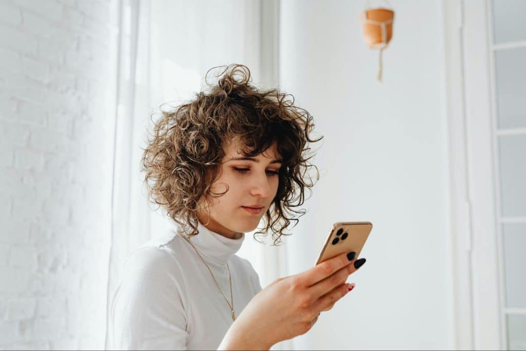 A woman with curly hair looking at a smartphone indoors.