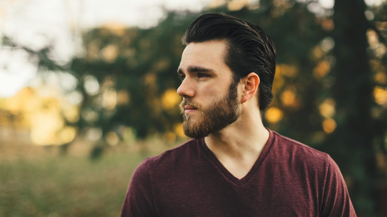 A man wearing a maroon v-neck t-shirt in the forest.
