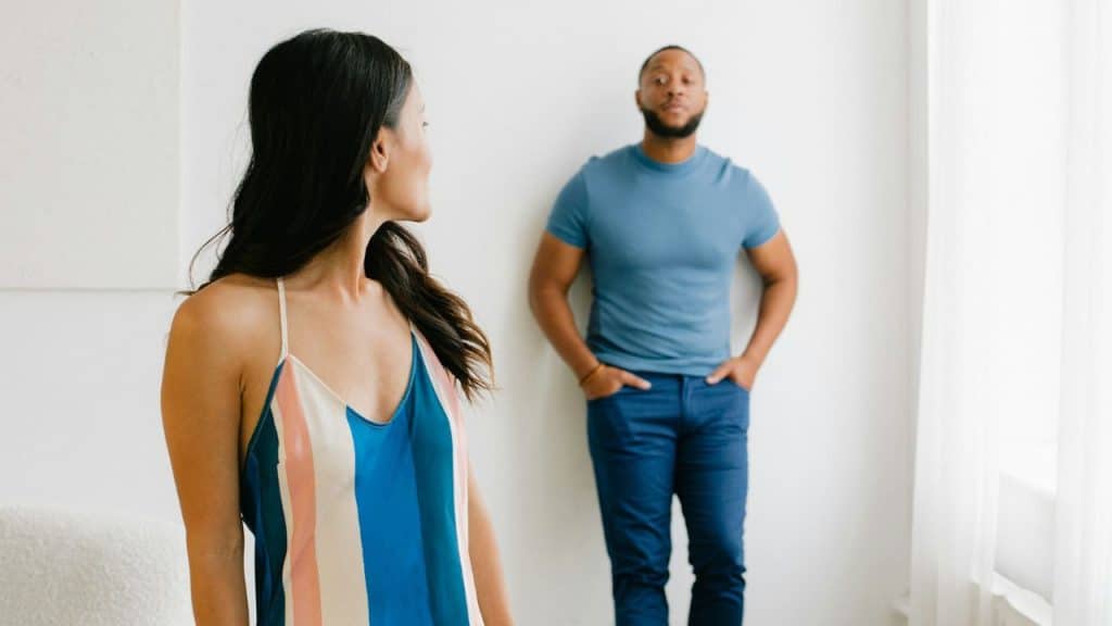 A woman looks over her shoulder at a man standing against a white wall.