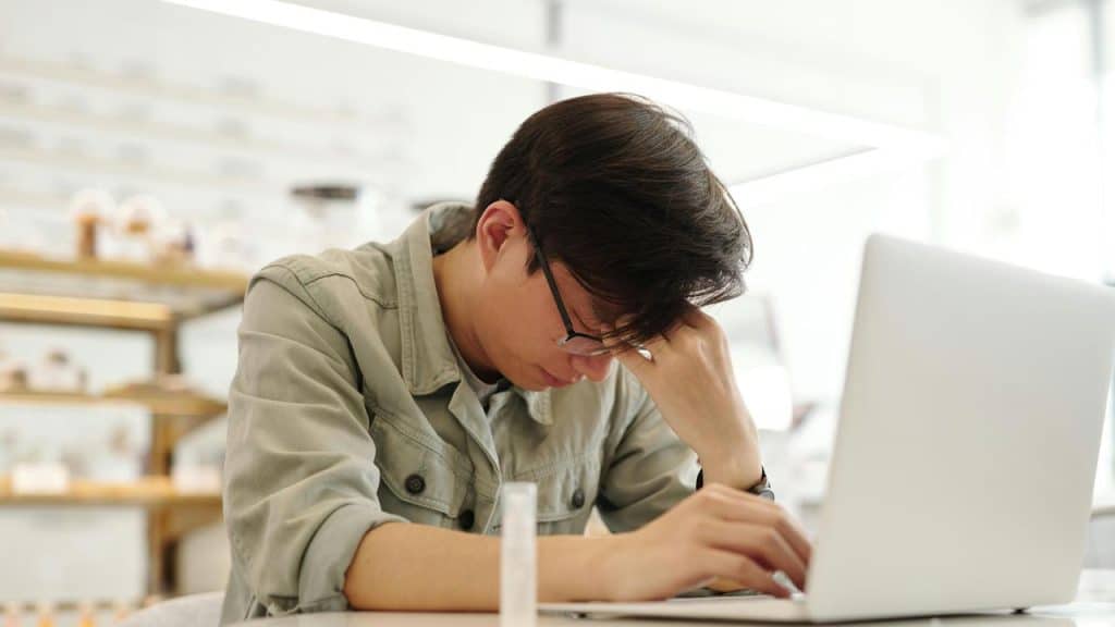 A tired man resting his head while using a laptop.