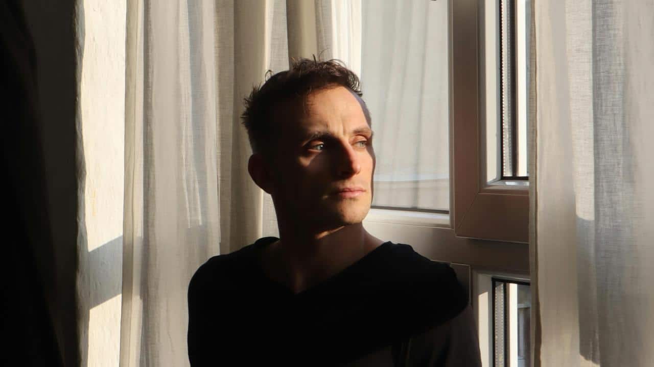 A man standing by a window with sunlight on his face.