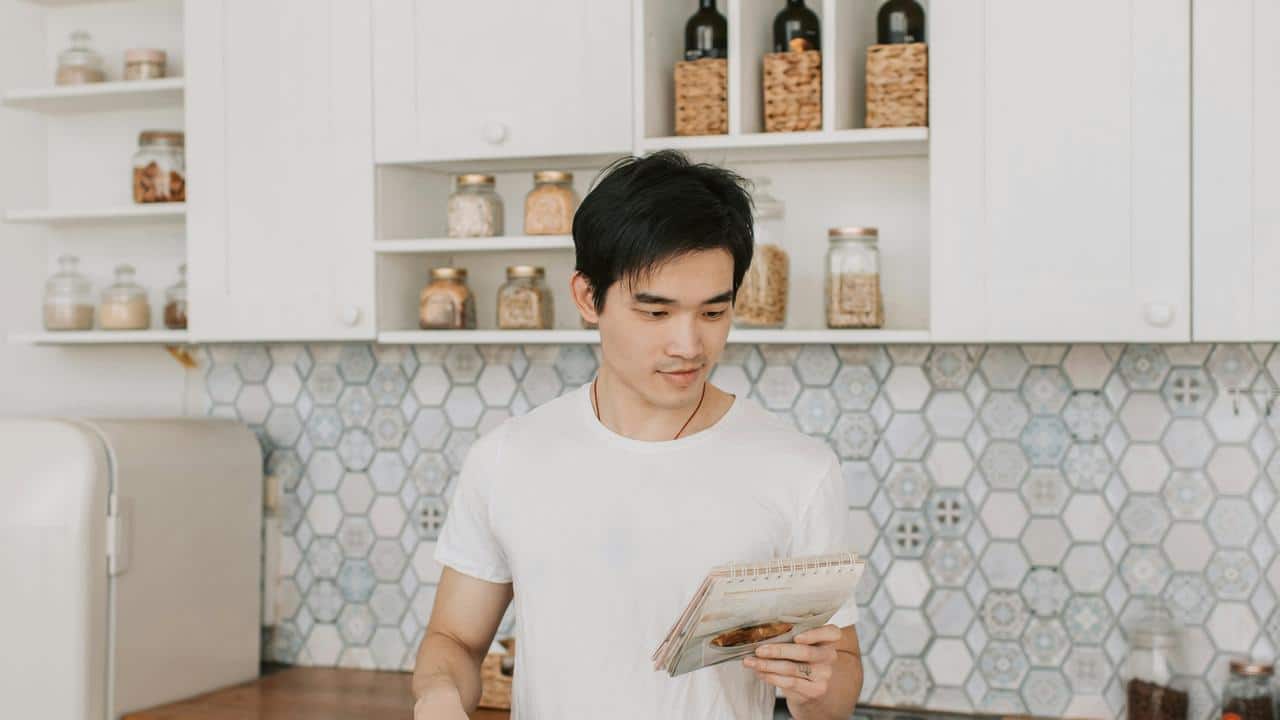 A person standing in a kitchen reading a recipe card.