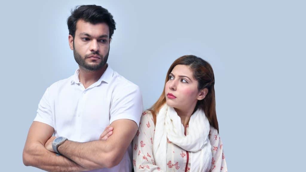 A man with crossed arms and a woman looking at him against a light background.