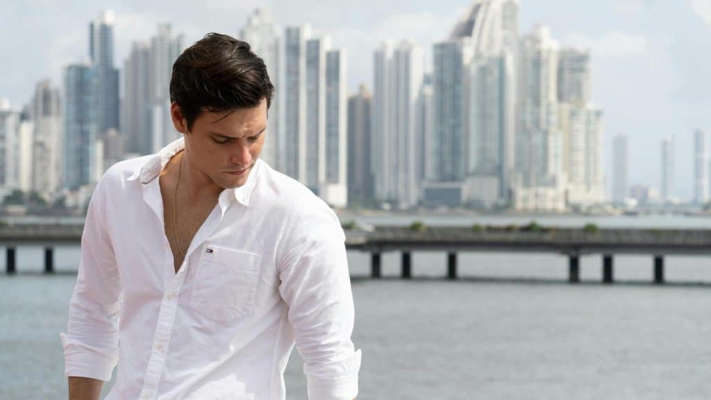A man in a white shirt looking down by the water.