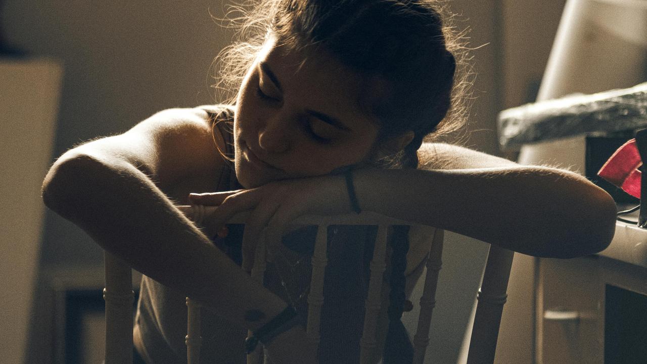 A tired woman resting her head on the back of a chair.