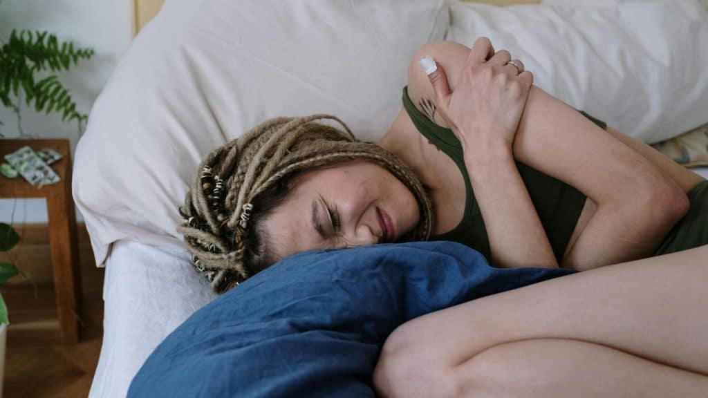 A woman lying on a bed holding her shoulder and wincing in pain.